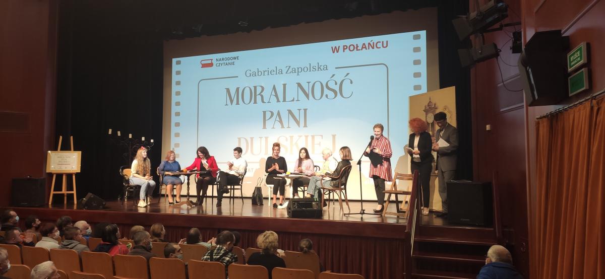 Zdjęcie kolorowe, Narodowe Czytanie Moralności Pani Dulskiej na sali widowiskowej Centrum Kultury i Sztuki w Połańcu, widoczni lektorzy na scenie