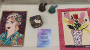 Zdjęcie kolorowe, fragment wystawy w Bibliotece pod hasłem Prace podopiecznych Środowiskowego Domu Samopomocy w Połańcu, eksponatami są ręcznie robione przedmioty użytkowe, obrazy i inne prace
