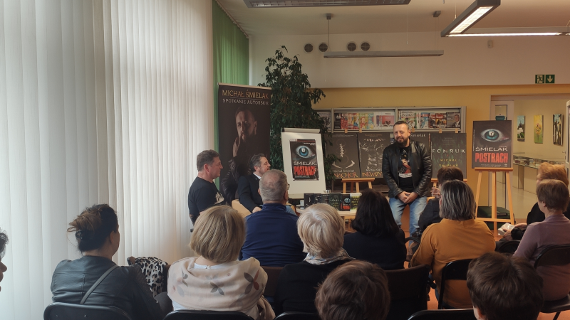 Zdjęcie kolorowe, uczestnicy spotkania autorskiego z pisarzem kryminałów Michałem Śmielakiem w Bibliotece